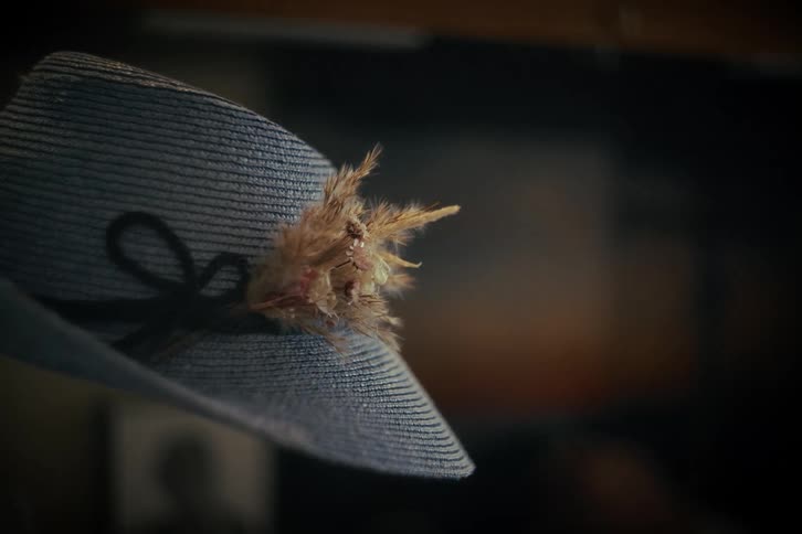 A close-up of a blue woven vintage-style hat with a feather and ribbon in a dimly lit setting