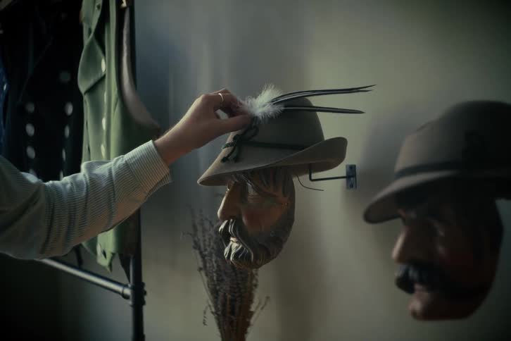 A person carefully places feathers into a traditional Bavarian hat resting on a carved wooden mask