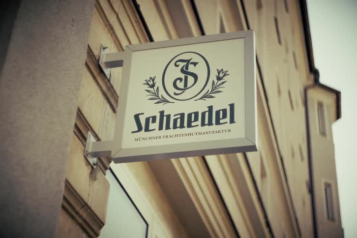 A classic, vintage-style sign for a traditional German hat maker hangs from a historic storefront