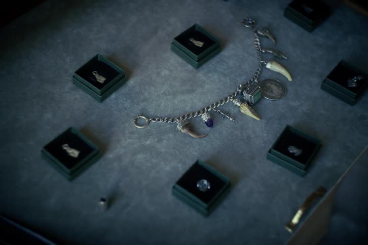 A hand slowly opens a wooden drawer to reveal a mysterious collection of antique jewelry, charms, and animal teeth