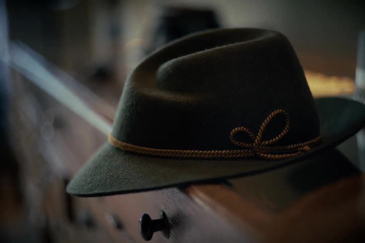 A close-up of a dark green felt fedora with a rope band resting on a wooden dresser as the focus slowly blurs
