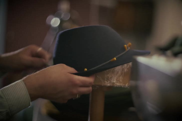 A skilled artisan hatter meticulously handcrafts a classic felt hat in his dimly lit, vintage-style workshop
