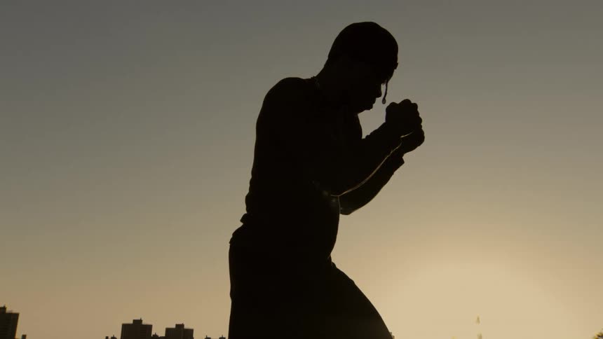 A powerful slow-motion silhouette of a boxer holding a defensive fighting stance at sunset
