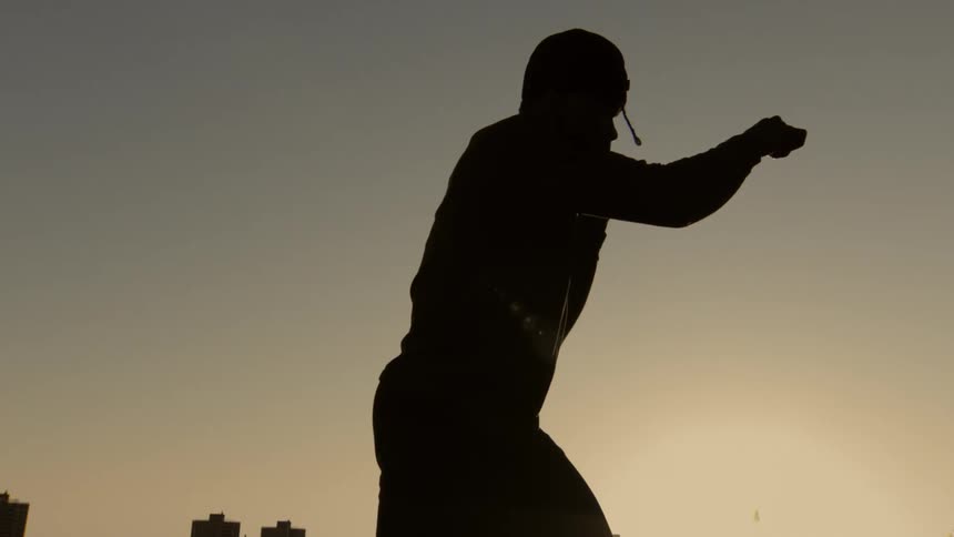 Slow motion silhouette of a boxer throwing a powerful punch with a city skyline in the background at sunset