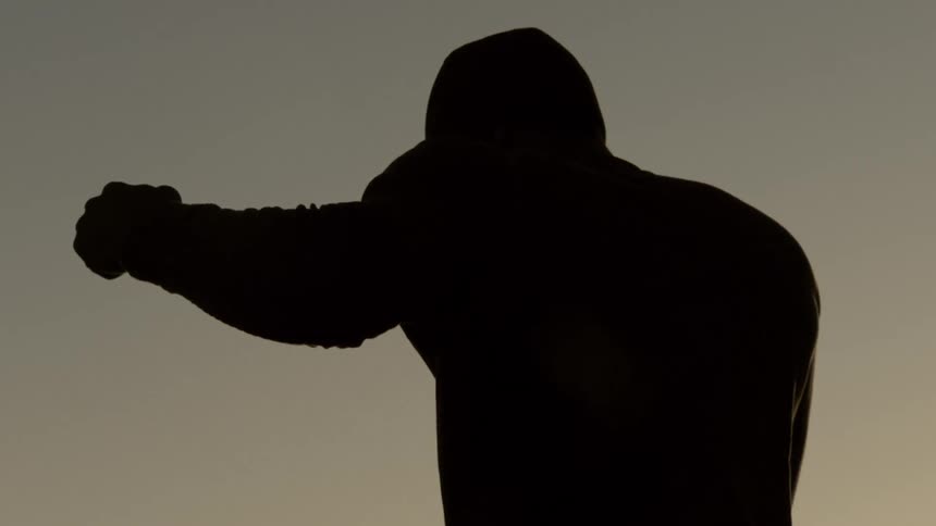 Close-up slow-motion silhouette of a man in a hoodie throwing a punch