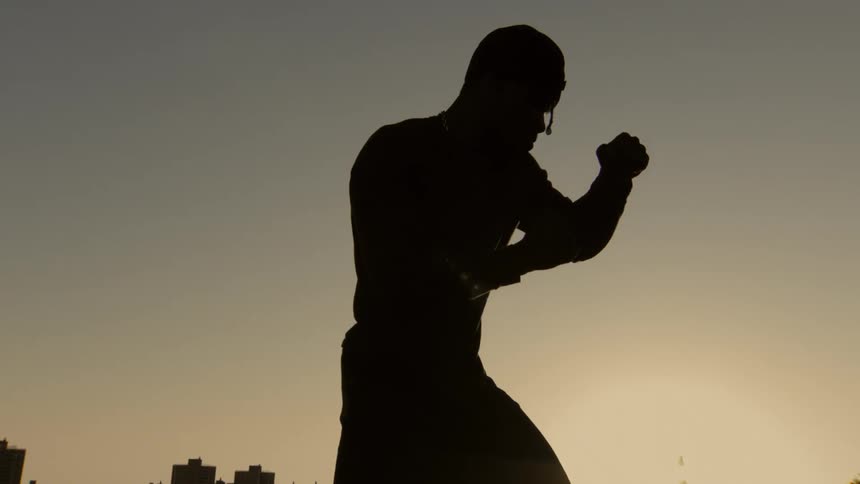 Dramatic slow motion silhouette of a fighter in a boxing stance against the sunset