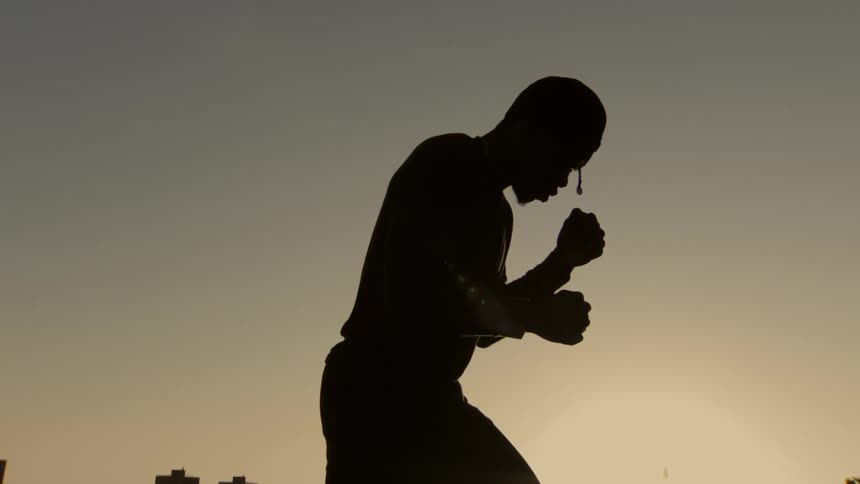 A slow-motion silhouette of a boxer wrapping his hands in preparation for a fight against the sunset sky