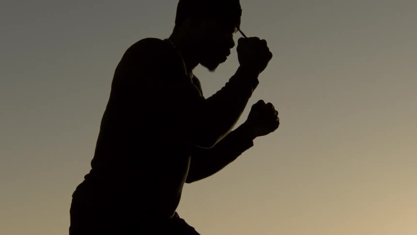 Slow-motion pull-out shot of a determined boxer's silhouette training against the New York City skyline at sunset