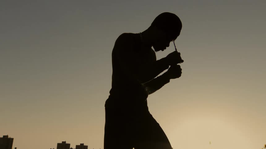 A dramatic slow-motion silhouette of a male boxer holding a defensive stance against the golden hour sky over the city