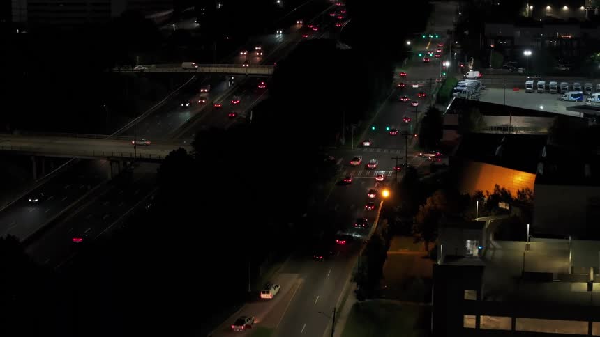 An aerial view shows the steady flow of traffic on a multi-lane highway and city streets under the darkness of night