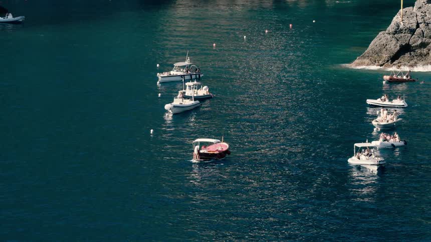 An idyllic scene of small tourist boats and yachts floating on the tranquil blue waters of a rocky Mediterranean cove on a sunny day