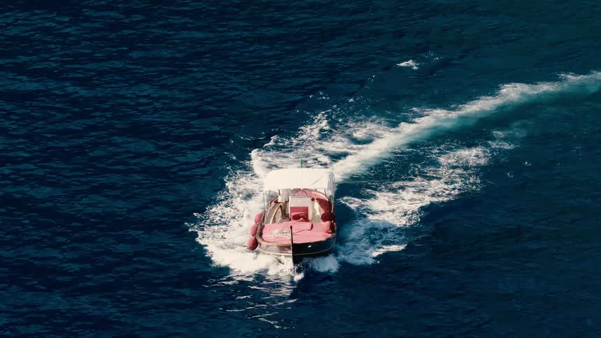Slow motion aerial shot of a classic Italian wooden boat making a turn on the deep blue Mediterranean sea