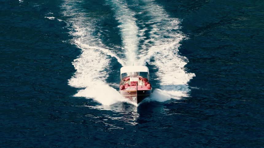 An elegant wooden motorboat travels through the deep blue ocean, filmed from above in super slow motion