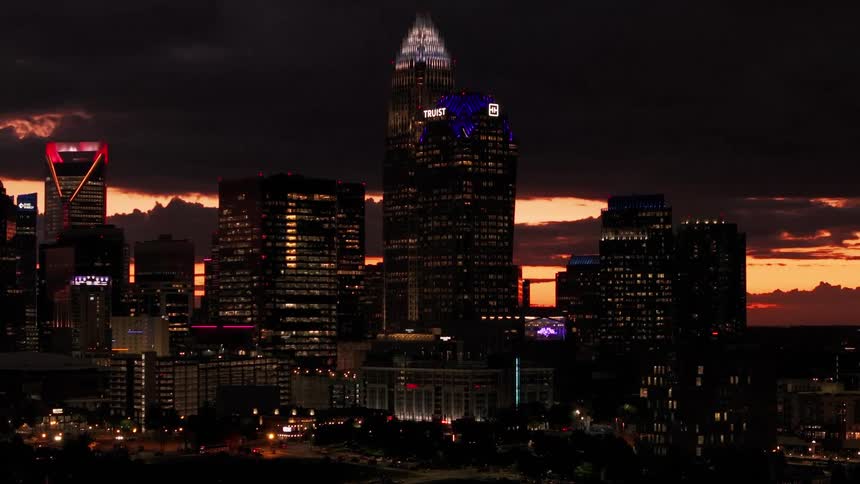 The illuminated skyline of Charlotte, North Carolina, glows beautifully against a dramatic orange sunset as the camera slowly pushes in