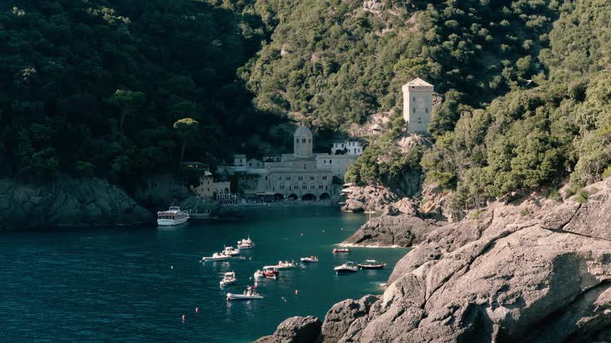 An aerial-style view reveals the picturesque San Fruttuoso Abbey and its secluded bay filled with boats on a sunny day along the Italian coastline