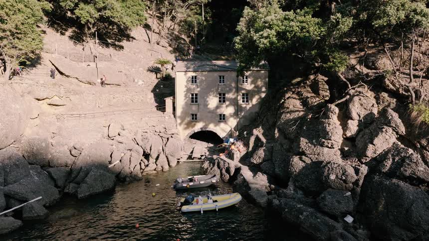 Aerial drone shot slowly approaches a historic stone building with a boat arch nestled in a secluded rocky cove