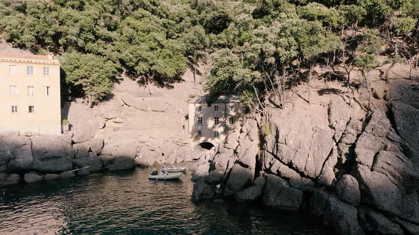 A serene view of a hidden cove with historic buildings nestled into rocky cliffs and small boats floating on the calm water