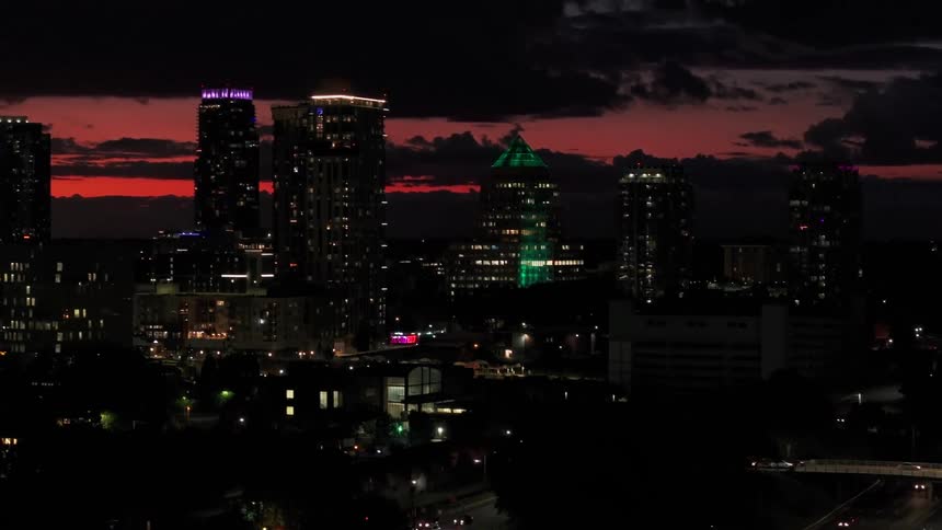 An aerial view of nighttime traffic tilting up to reveal the city skyline of Tampa, Florida, against a vibrant red sunset