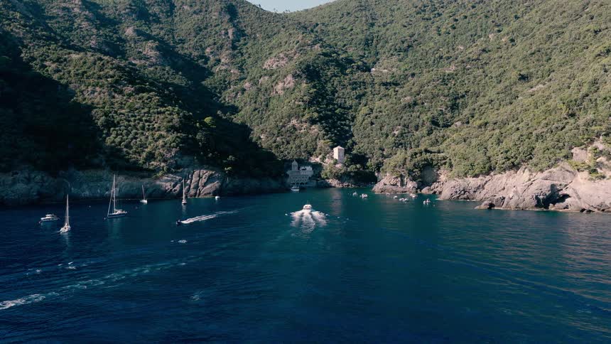 Aerial view of yachts and boats cruising in the serene blue waters of a secluded bay nestled among lush green coastal mountains