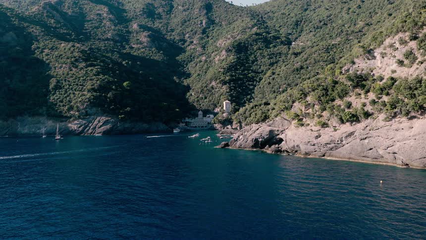 A stunning aerial view of the deep blue sea along the rugged, green coastline of Italy, with boats dotting the tranquil water