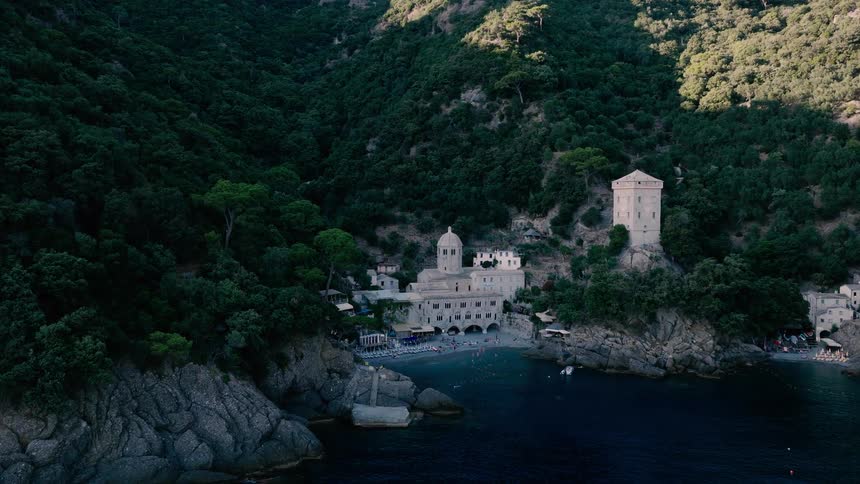 Aerial drone footage slowly approaches the historic San Fruttuoso Abbey tucked away in a lush green cove on the Italian Riviera