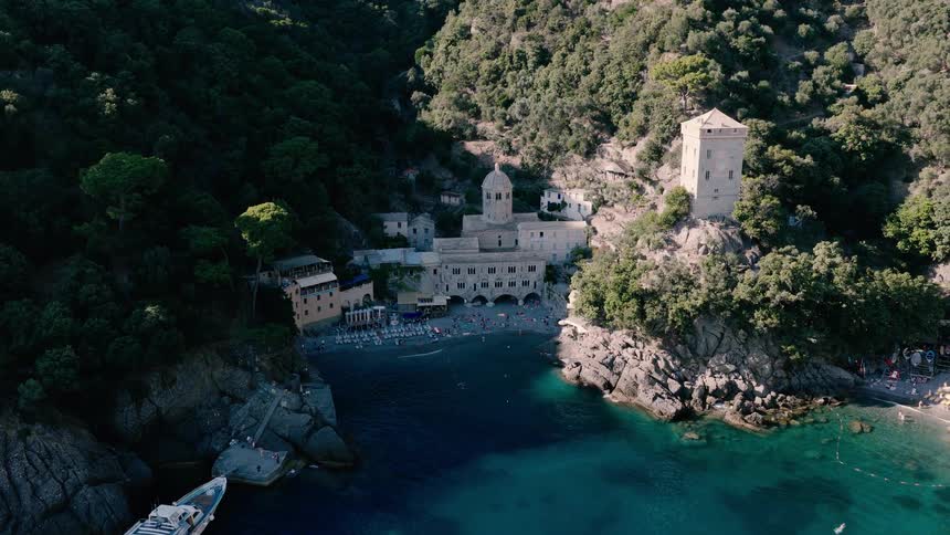 An aerial view of the historic San Fruttuoso Abbey nestled in a secluded Italian cove where tourists swim and relax on the beach