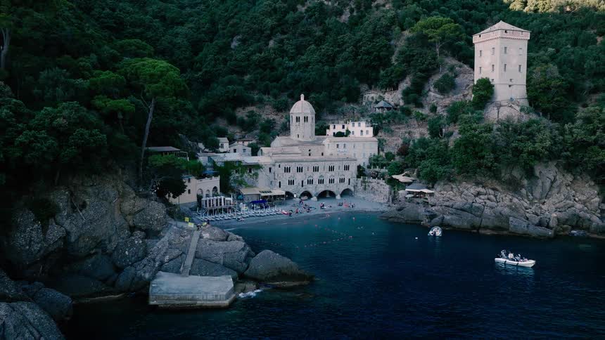 Aerial view slowly pulls back from the historic Abbey of San Fruttuoso to reveal the secluded cove filled with beachgoers and boats