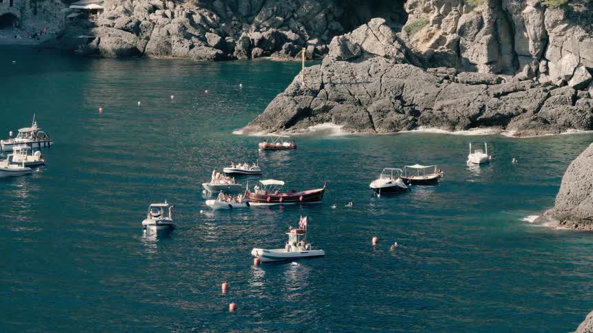 Tourists enjoy a sunny day on small boats and swimming in the calm, blue waters of a picturesque Italian coastal cove
