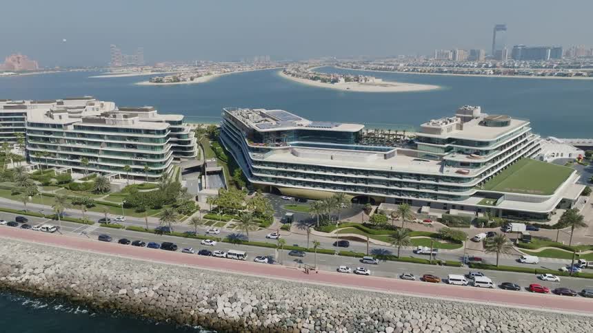 A static aerial view of the W Dubai - The Palm hotel, showcasing its modern design against the backdrop of the Palm Jumeirah and a busy coastal road