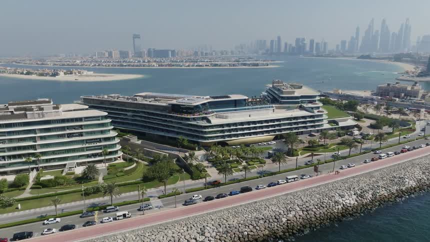 Stationary aerial view of the luxurious W Dubai - The Palm hotel, with the city skyline and Palm Jumeirah in the background on a sunny day