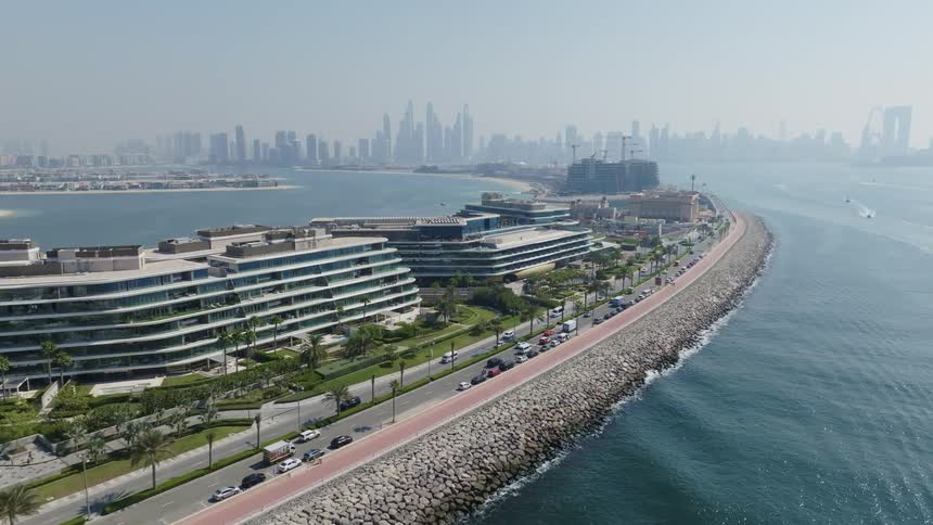A static aerial view over the Palm Jumeirah crescent in Dubai, with modern hotels and a coastal road next to the ocean and the city skyline in the distance