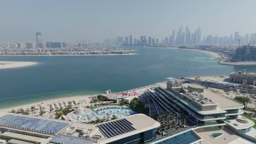 An aerial view pushes in on a luxury hotel on the Palm Jumeirah, revealing pools and a private beach with the Dubai skyline in the background