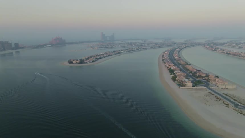 An expansive aerial shot captures the iconic Palm Jumeirah island in Dubai during a hazy sunrise