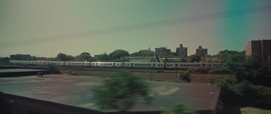 A stylized tracking shot from a moving vehicle captures a parallel passenger train traveling through an urban industrial area