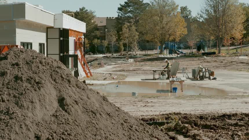 Wide shot of construction workers on a muddy job site next to a partially completed modern building