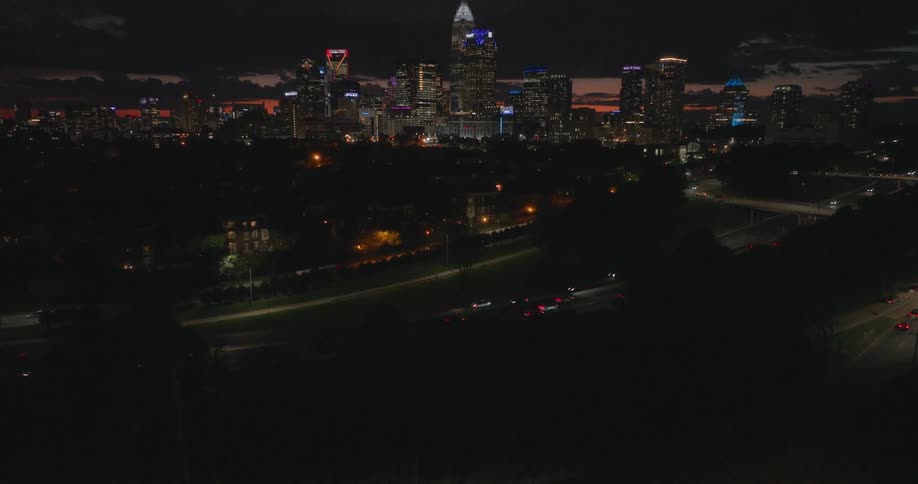 A dramatic aerial shot pushes forward and tilts up from darkness to reveal the glowing Charlotte, North Carolina city skyline at night