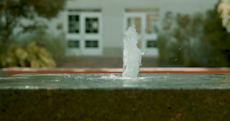 A slow motion close-up of a single water jet bubbling in a fountain within a tranquil courtyard