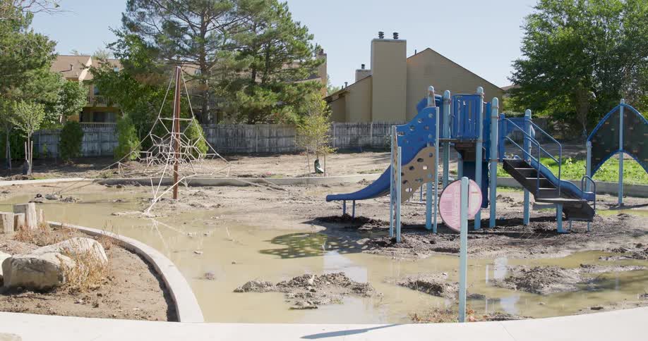 Slow zoom out from a children's playground destroyed and covered in mud and water after a flood