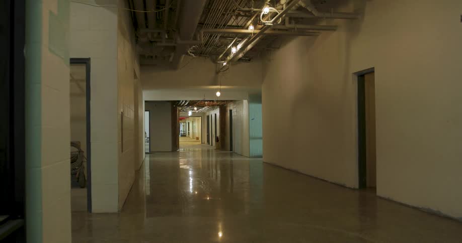 A slow reveal of a long, empty building hallway under construction with polished floors and exposed ceiling pipes