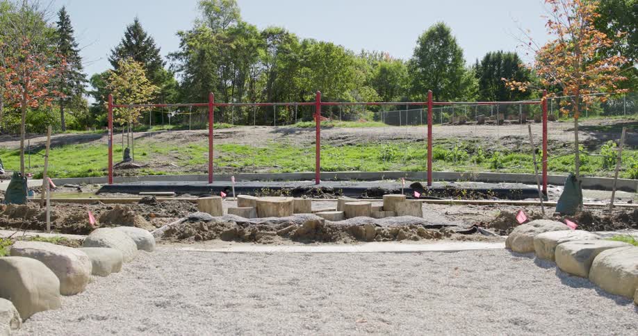 A static wide shot of a new natural playground with wooden stumps and a gravel path under construction in a park