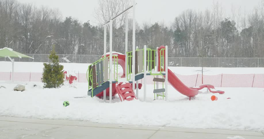 A colorful children's playground sits empty and covered in a blanket of fresh snow as more snow falls