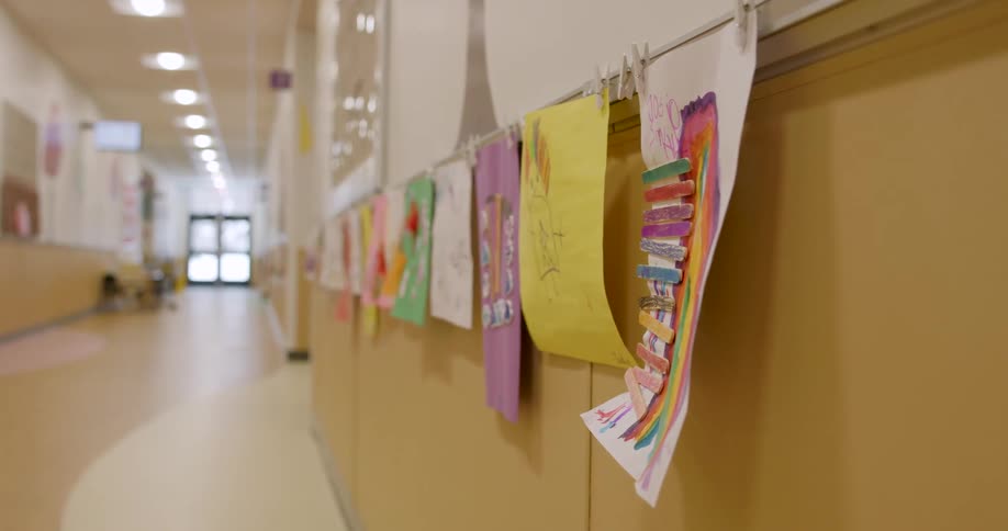 Children's colorful artwork is clipped to a line hanging on the wall of a quiet school hallway