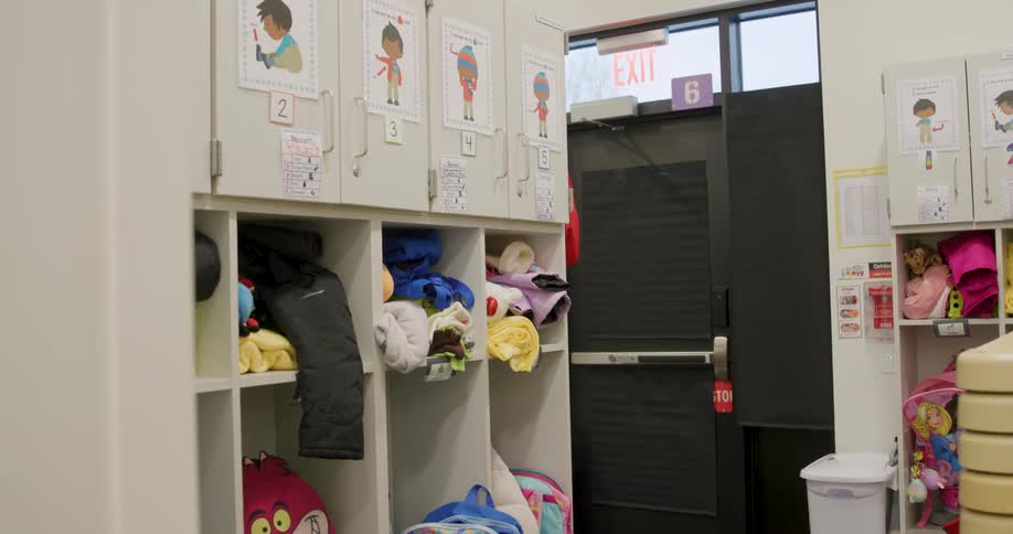 A slow reveal of a row of cubbies in a daycare or preschool filled with children's backpacks and belongings
