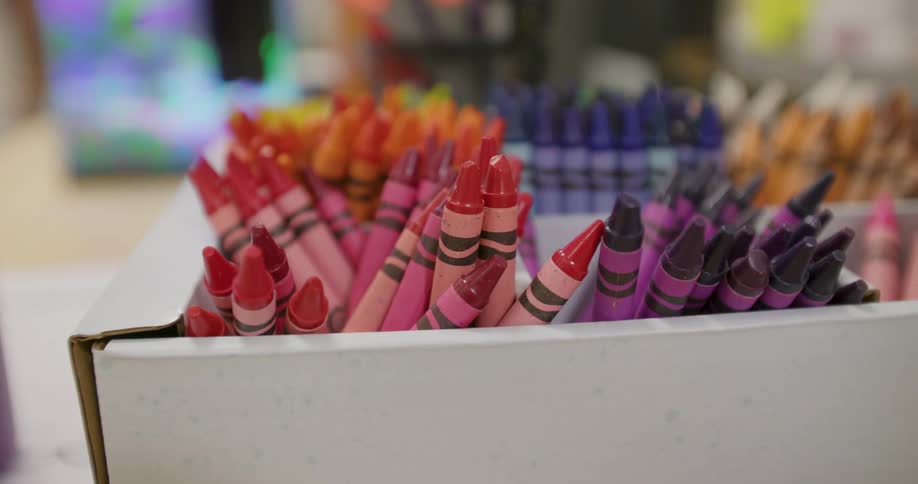 A slow pull-back shot reveals a box filled with a vibrant assortment of colorful crayons