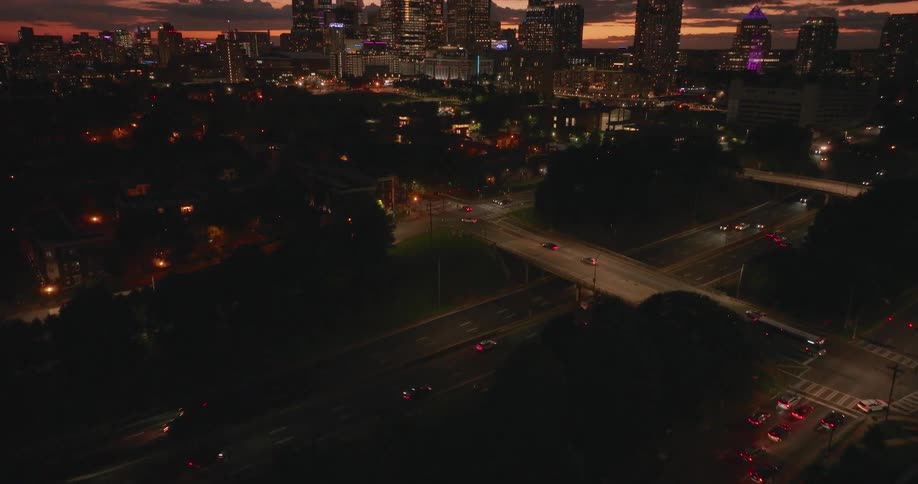 Aerial camera tilts up from a dark parking lot to reveal the glowing Charlotte, North Carolina city skyline at sunset