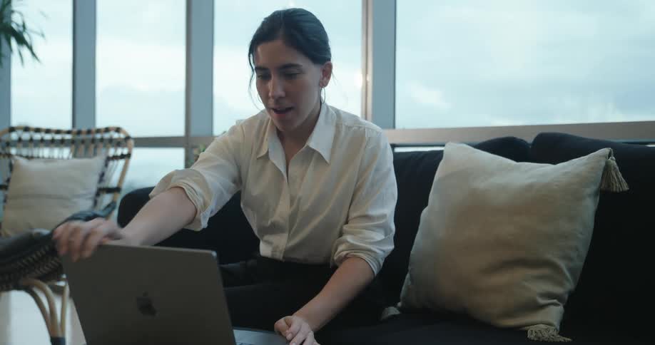 A professional woman opens her laptop and starts working while sitting on a couch in a modern high-rise office space