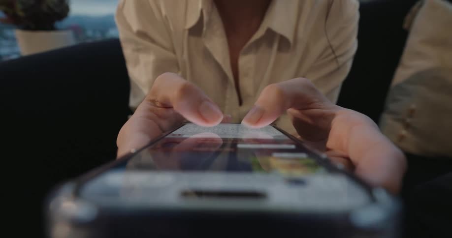 A low-angle close-up shot shows a person's hands rapidly typing and scrolling on a brightly lit smartphone screen