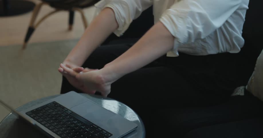 A woman opens her laptop on a small table, stretches her hands, and then begins typing on the keyboard