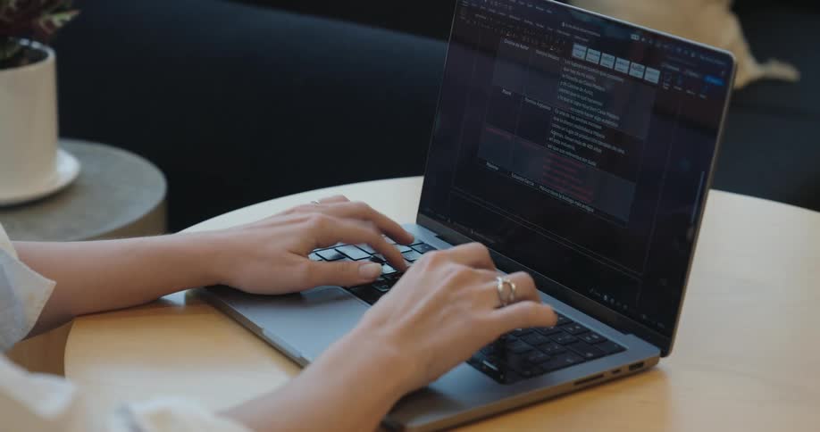 A close-up, over-the-shoulder view shows a person's hands diligently typing on a laptop keyboard