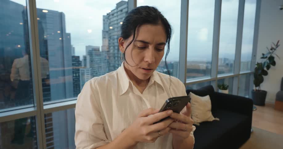 Slow push-in on a worried woman reacting to bad news on her smartphone in a modern high-rise office